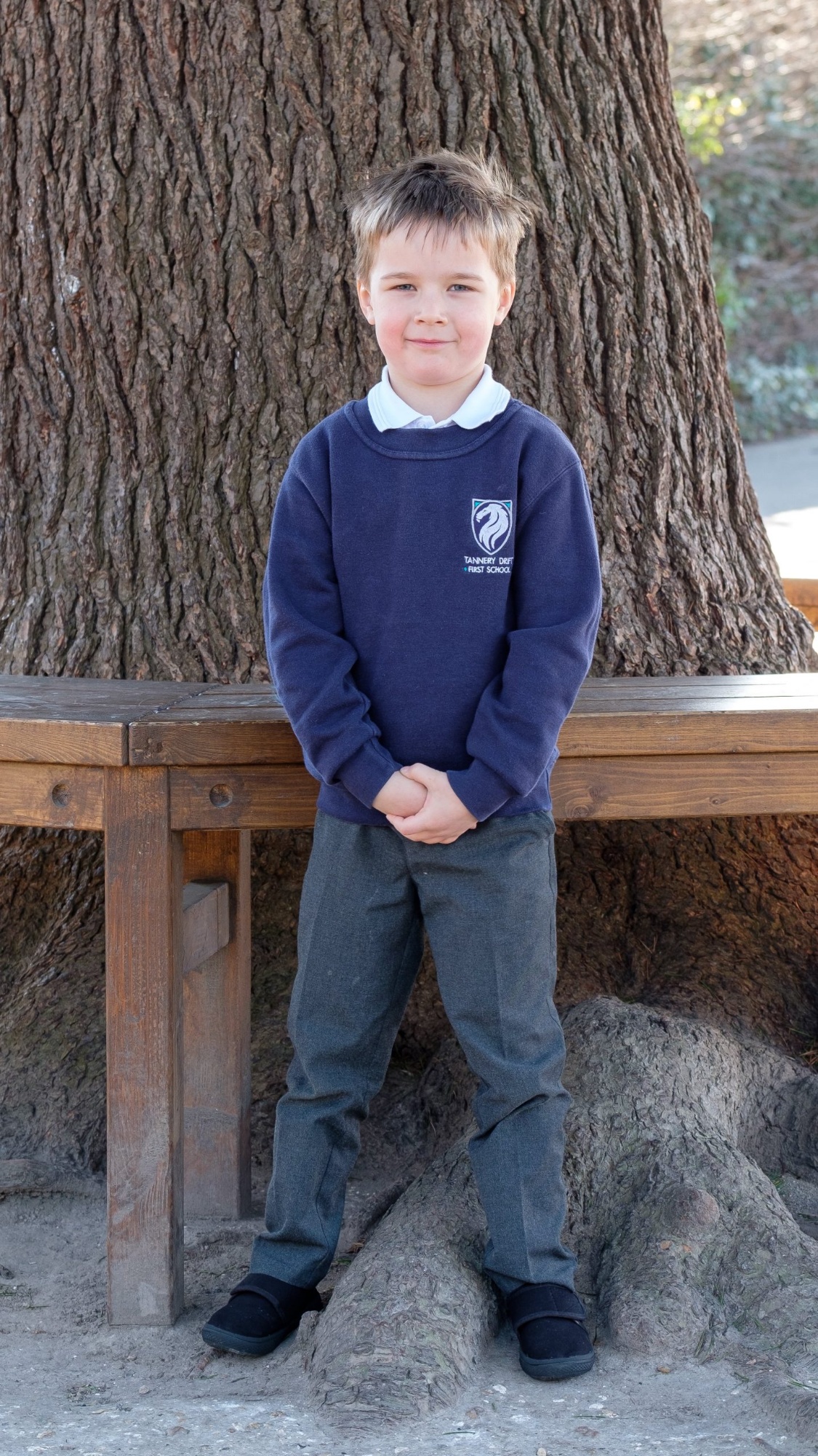 A male pupil stands outside wearing his school uniform, consisting of trousers, a white polo shirt and a school jumper